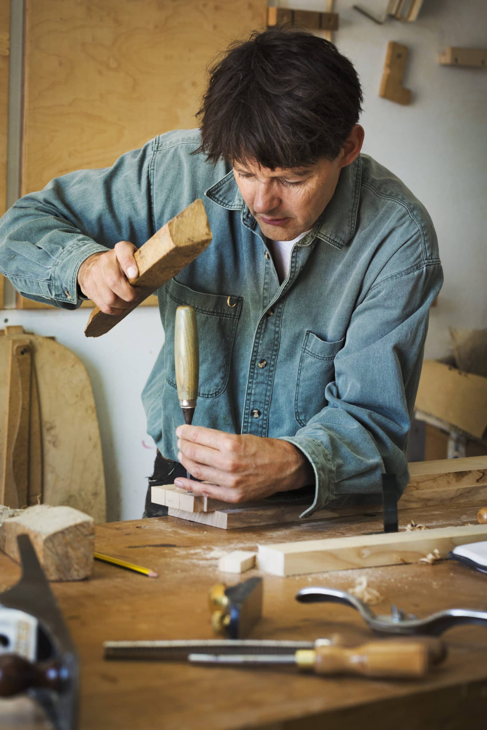 A craftsman using a piece of wood on the end of a chisel to mark a piece of wood 